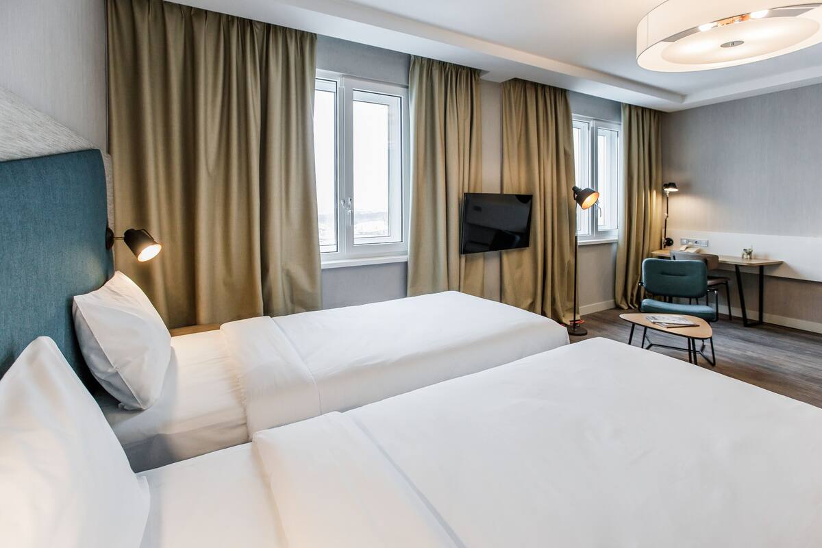 A hotel room with two beds, a TV, a desk, and a chair.