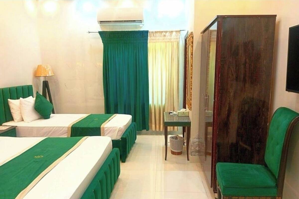 Ein Hotelzimmer mit zwei Betten, einem grünen Sessel, einem Holzschrank und einem kleinen Tisch.
