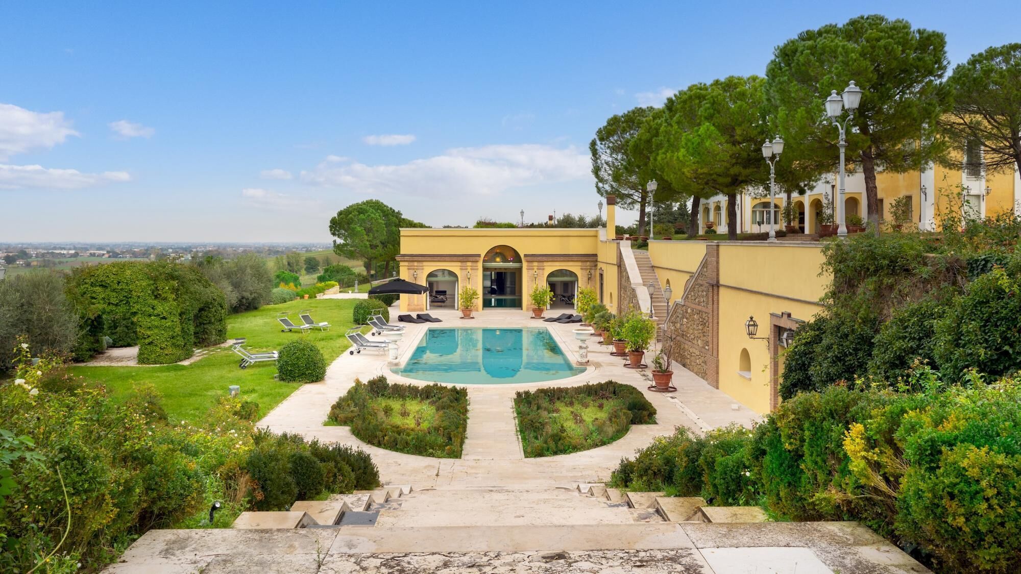 A pool area with a view of a building with arches and a garden.