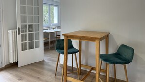 Una habitación con una mesa de madera y dos sillas verdes, un radiador blanco y un ventanal de vidrio que da a otra estancia.