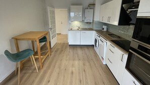 Una cocina compacta con una mesa y sillas de madera, lavadora, estufa y una lámpara en el techo.