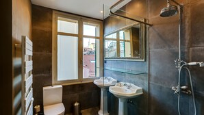 A modern bathroom with a toilet, two sinks, and a shower.