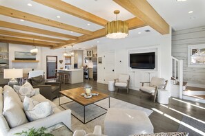 A spacious living area with a large island, a kitchen in the background, and a TV mounted on the wall. - Walk to Beach | Carriage House (Inlet Beach)