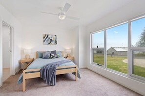 Une chambre à coucher avec un lit, des tables de chevet, un ventilateur de plafond, une fenêtre donnant sur un beau paysage et un tableau accroché au mur.