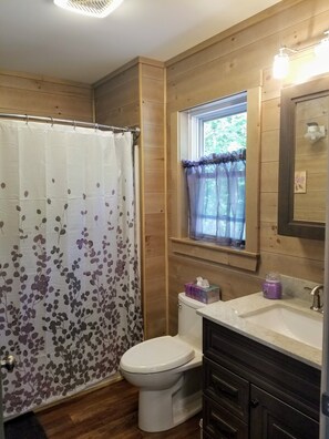 A bathroom with a shower curtain, toilet, sink, and window with curtains.