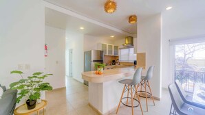 A modern kitchen with a central island, bar stools, and a view of the living area. - Walk to 5th Ave & Beach · Pools, Balcony & Parking (Playa del Carmen)