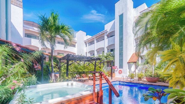 A hotel pool area with a hot tub, surrounded by lush greenery and a clear blue sky. - Walk to 5th Ave & Beach · Pools, Balcony & Parking (Playa del Carmen)