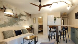 A modern living room with a sofa, coffee table, and bar stools. There is a ceiling fan, a kitchen area, and a small dining table. - Air-conditioned apartment 3 minutes' walk from the beach and shops (Bormes-les-Mimosas)
