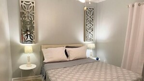 A bedroom with a bed, two bedside tables, a wall-mounted light fixture, and a decorative wall panel. - Ocean Getaway - Ocean Front Condo (North Topsail Beach)