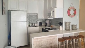 A kitchen with white cabinets, a white refrigerator, a microwave, a stove, and a bar area with stools. - Ocean Getaway - Ocean Front Condo (North Topsail Beach)