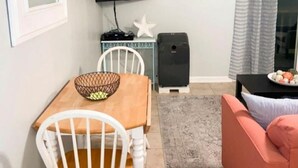 A living room with a wooden dining table, white chairs, a television mounted on the wall, a speaker, and a pink sofa. - Ocean Getaway - Ocean Front Condo (North Topsail Beach)