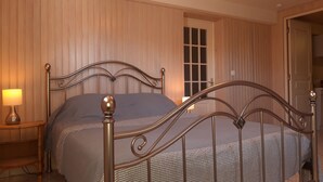 Un dormitorio con estructura de cama metálica, una mesita de noche con lámpara y una ventana con persianas.