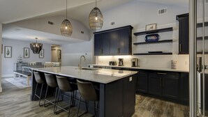 A modern kitchen with a central island, bar stools, pendant lighting, and dark cabinetry.