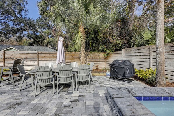 Un patio con sillas Adirondack, una parrilla y una piscina.