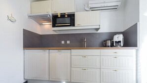 A modern kitchen with white cabinetry, a built-in oven, a coffee machine, and a stainless steel sink. - Florella Residences Studio terrasse Maréchal Joffre (Cannes)