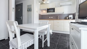 A modern kitchen with white cabinets, a microwave, a coffee maker, and a flat-screen TV. - Florella Residences Studio terrasse Maréchal Joffre (Cannes)