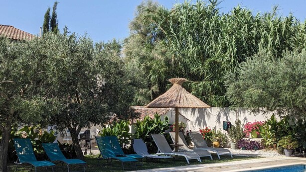 Una piscina con sillones de descanso y una sombrilla de paja.
