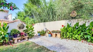 Un jardín con un camino de grava, plantas en macetas y una pared blanca.