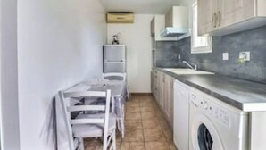 Una cocina compacta con lavadora, un pequeño comedor con sillas y piso de baldosas.