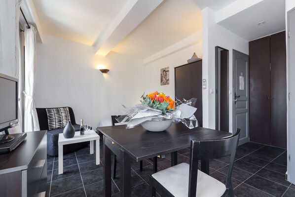 A modern dining area with a dark wooden table, white chairs, and a vase of orange flowers.