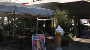 An outdoor seating area with tables and chairs, a sign for Roter Faden restaurant, and a large ice cream cone sculpture. - Comfort-Deluxe-Apartment (Hannover)