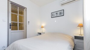 Un dormitorio con cama, dos mesitas de noche con lámparas, una puerta con panel de vidrio y un aire acondicionado de pared.