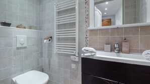Un baño moderno con inodoro blanco, toallero blanco, espejo sobre el lavabo y mueble de tocador oscuro.