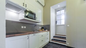 Una cocina con armarios blancos, microondas, cafetera y pileta. Hay escalones que llevan a una puerta.