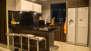 A modern kitchen with a central island, bar stools, a refrigerator, and a window with blinds.