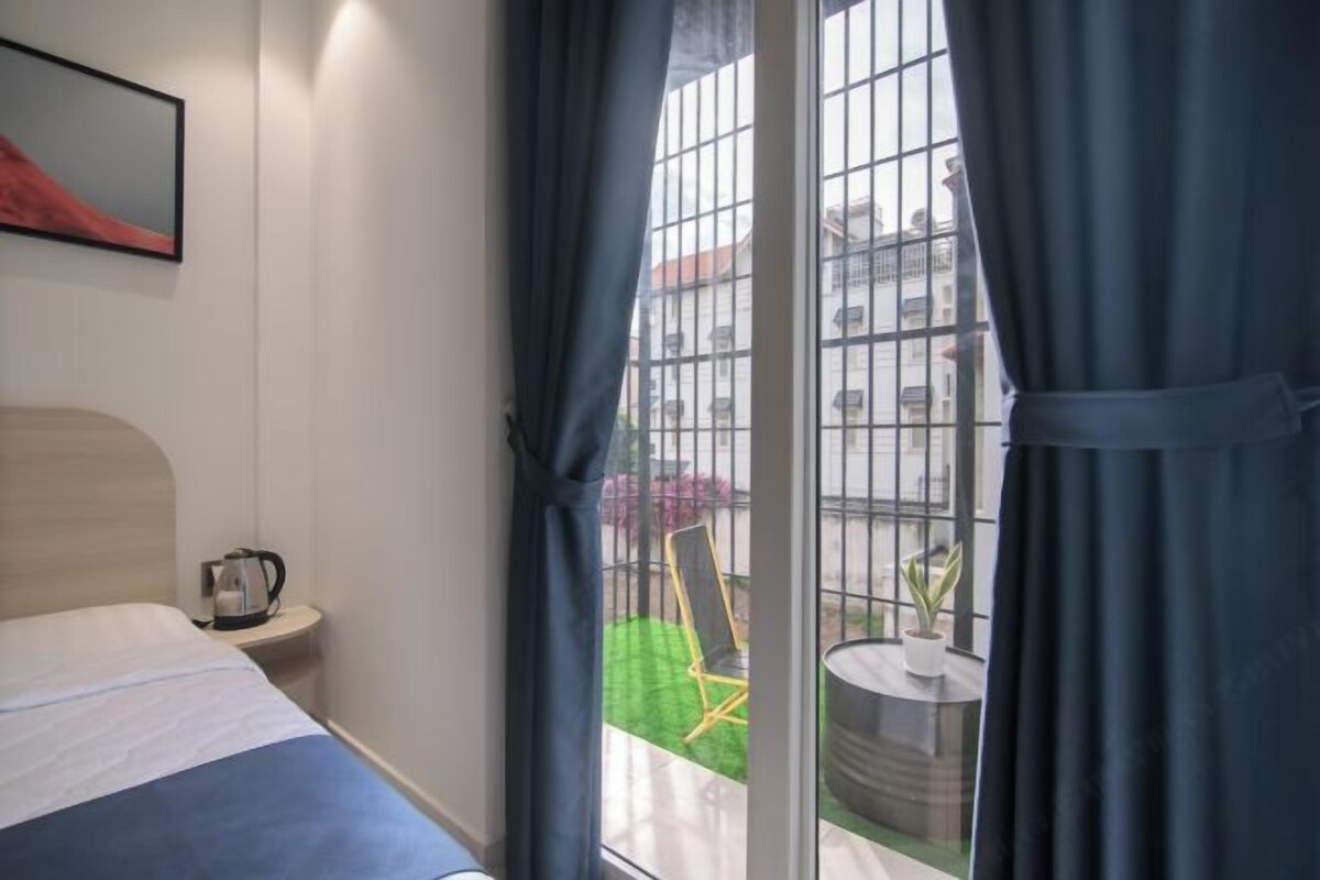 Ein Hotelzimmer mit Bett, Nachttisch, Wasserkocher und Blick auf einen Balkon mit Stuhl und Tisch.