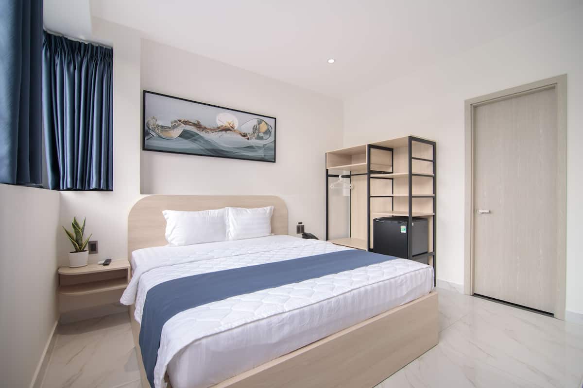 Quarto de hotel moderno com uma cama grande, mesa de cabeceira com planta, obra de arte na parede e estantes embutidas.