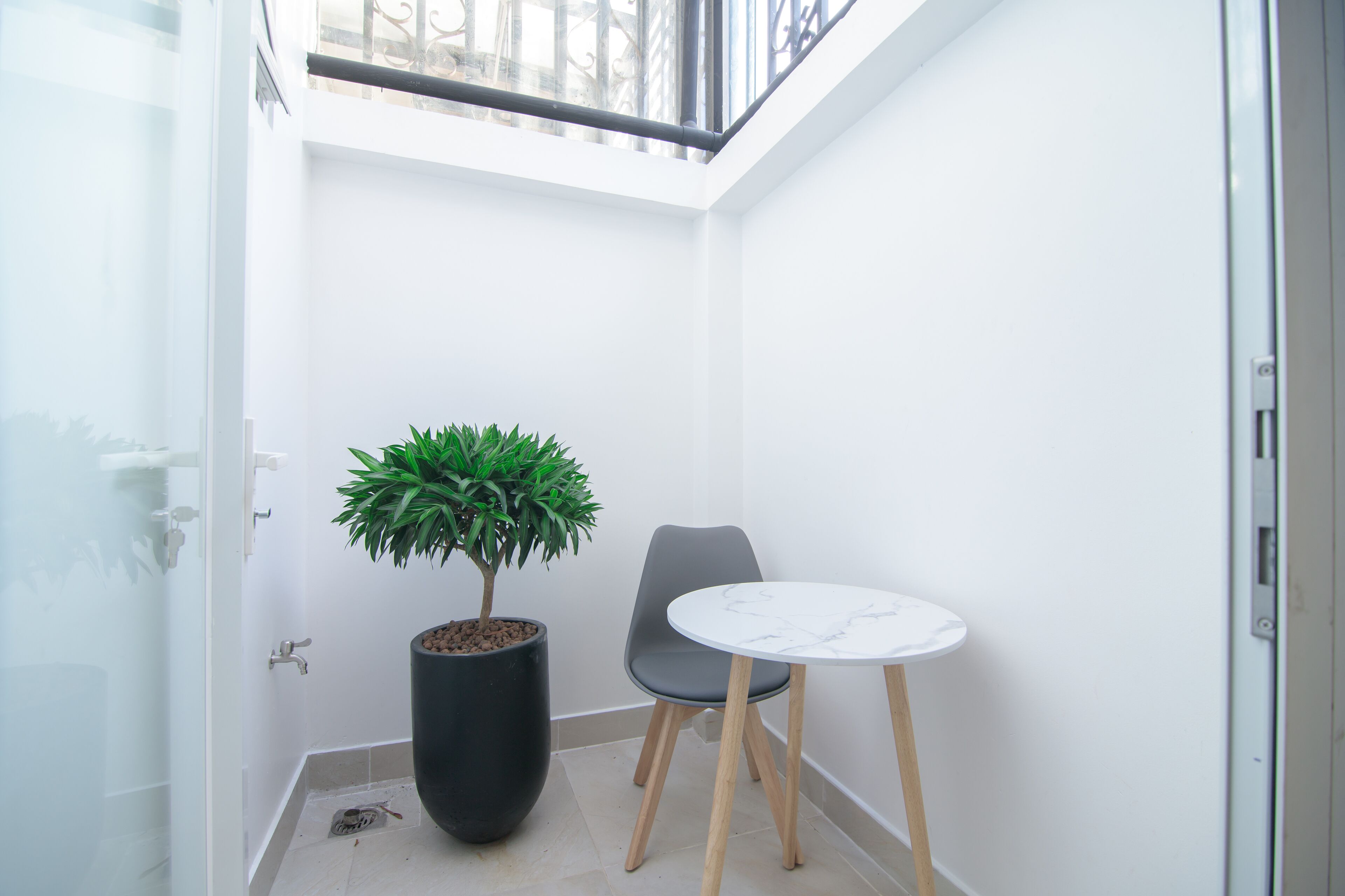 A small, enclosed balcony with a potted plant, a chair, and a round table.