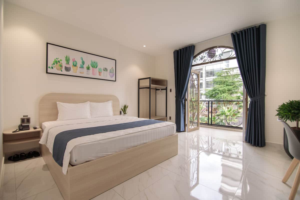 Une chambre à coucher moderne avec un grand lit, une table de chevet, une plante décorative et une vue sur l’extérieur.