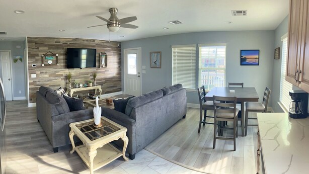 A modern kitchen with a built-in oven, a dining area with a wooden table and chairs, a gray sofa, and a ceiling fan. - Hackberry Hideaway III (Hackberry)
