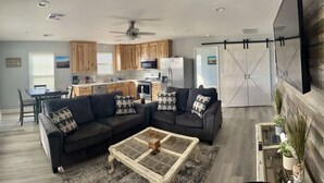 A modern living room with a sectional sofa, a coffee table, and a kitchen in the background. - Hackberry Hideaway III (Hackberry)