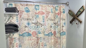 A bathroom with a toilet, a sink, and a shower curtain with ocean-themed designs. - Hackberry Hideaway III (Hackberry)
