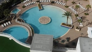A large circular pool with multiple lounge areas and palm trees.