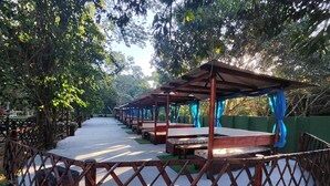 A row of wooden benches with blue curtains, set against a backdrop of trees and a clear sky. - Clube Pousada Chácara da Isabel (Águas Lindas de Goiás)