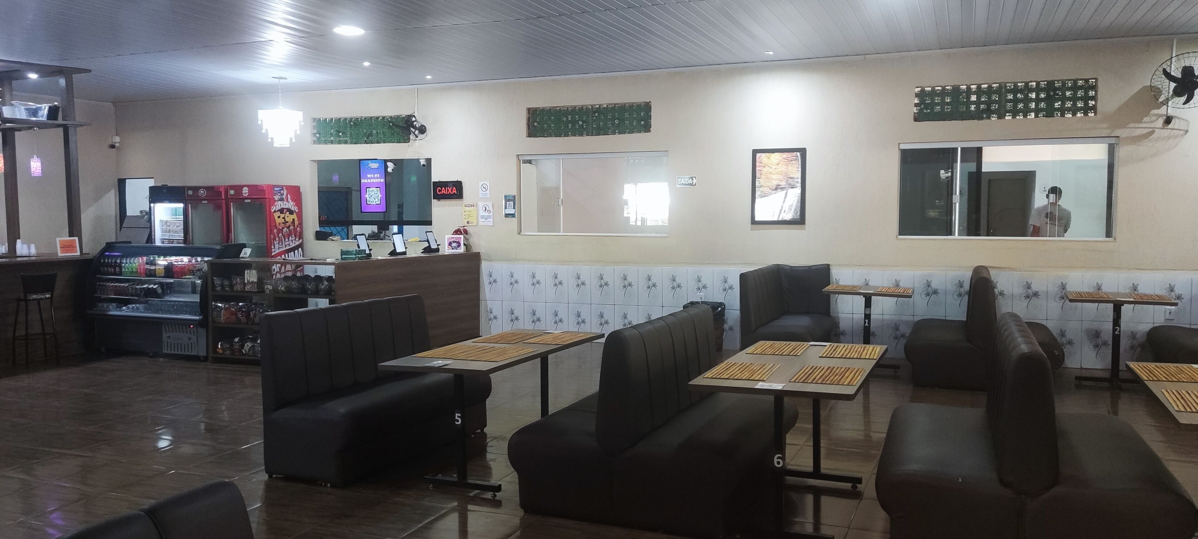 A restaurant with booths and tables, a counter with a cash register, and a television screen.