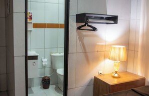 Ein Badezimmer mit Toilette, Mülleimer, Handtuchhalter und Nachttisch mit Lampe.