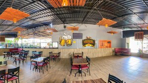 A spacious indoor dining area with wooden tables and chairs, a high ceiling with exposed beams, and a mural of beer mugs on the wall. - Clube Pousada Chácara da Isabel (Águas Lindas de Goiás)
