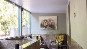 A seating area with a marble bench and wicker chairs, a large window with blinds, and a painting of a lion on the wall. - Clube Pousada Chácara da Isabel (Águas Lindas de Goiás)
