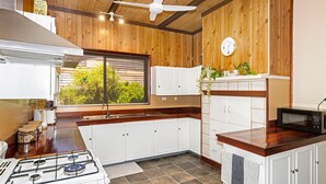 Cucina con pareti in legno, fornello a gas, mobili bianchi, microonde e una finestra con vista sul verde.