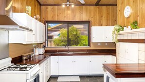 Una cucina con mobili bianchi, un fornello, una finestra che si affaccia sul verde e una sveglia appesa al muro.