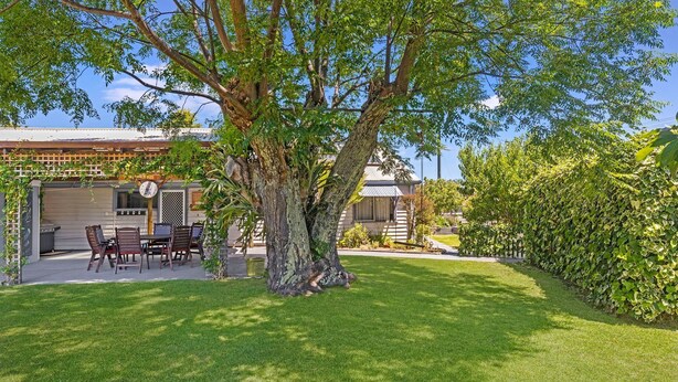 Un cortile con tavolo e sedie, un albero grande e una casa con garage.