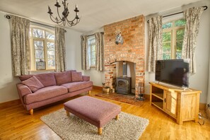 A living room with a brick fireplace, a sofa, an ottoman, a television on a wooden stand, and a chandelier. - Family home in the countryside - Pass the Keys (Lincoln)