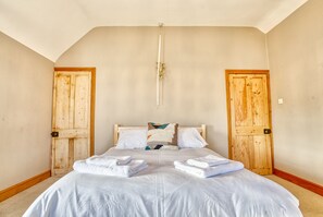 Une chambre à coucher avec un grand lit, deux portes en bois et un luminaire fixé au plafond.