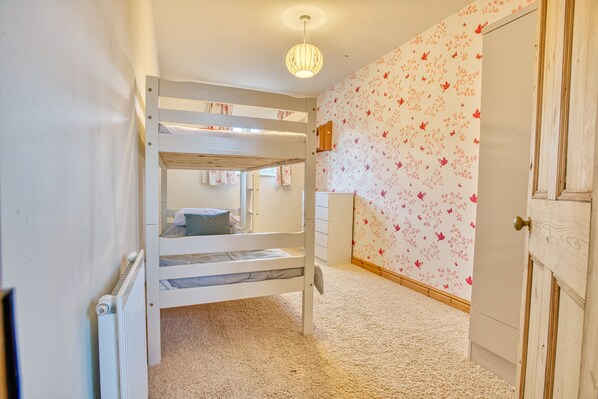 Une chambre avec un lit superposé, un radiateur, une armoire en bois et un papier peint à motifs floraux.