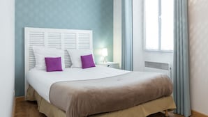 Una cama bien hecha con cabecera blanca, dos almohadas moradas y colcha marrón.