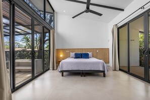 A modern bedroom with a large bed, a ceiling fan, and a view through glass doors to an outdoor area. - Open Living Style Home 1Km From Beach (Potrero)